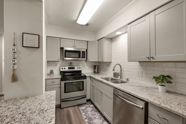 kitchen featuring a sink, a textured ceiling, backsplash, crown molding, and appliances with stainless steel finishes