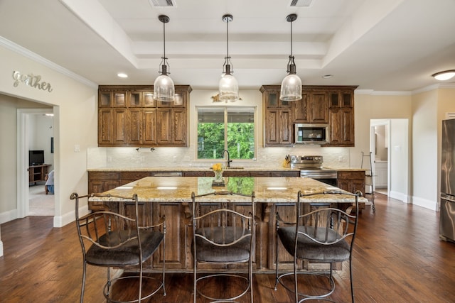 kitchen with a raised ceiling, appliances with stainless steel finishes, a center island, and decorative backsplash