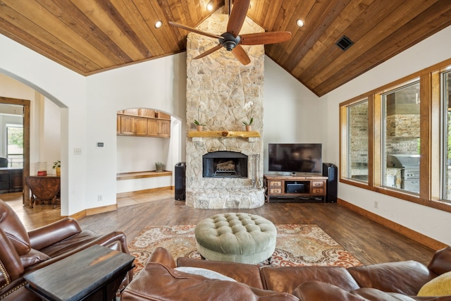 living area featuring a stone fireplace, wood finished floors, a ceiling fan, wooden ceiling, and arched walkways