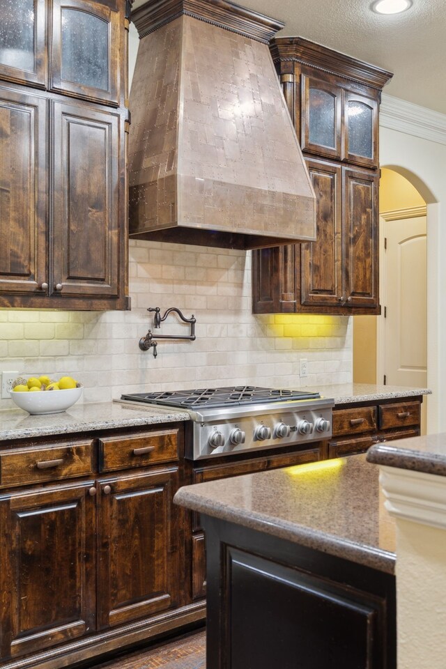 4401 Sorrel Ct, Flower Mound, TX 75028 - kitchen with stainless steel gas stovetop, custom exhaust hood, arched walkways, dark brown cabinetry, and ornamental molding