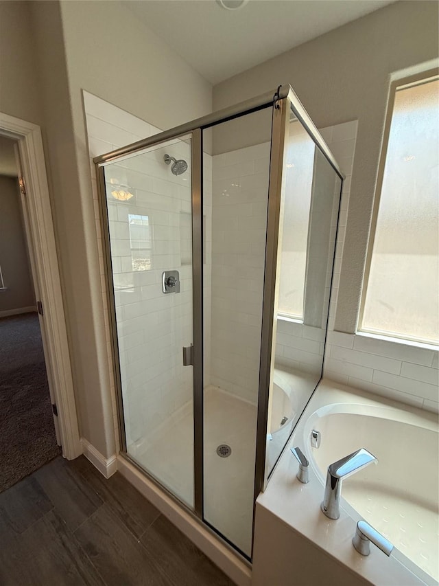 full bathroom featuring a stall shower, a garden tub, and wood finished floors