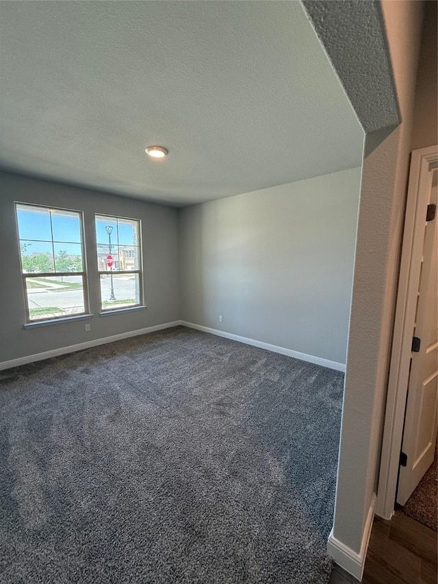 empty room featuring baseboards, dark colored carpet, and a textured ceiling