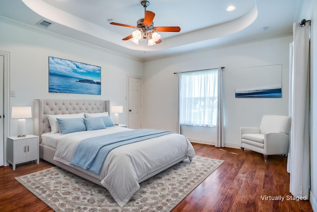 bedroom featuring a tray ceiling, visible vents, baseboards, ornamental molding, and wood finished floors