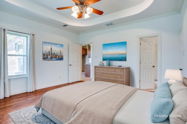 bedroom with visible vents, ornamental molding, wood finished floors, and a tray ceiling