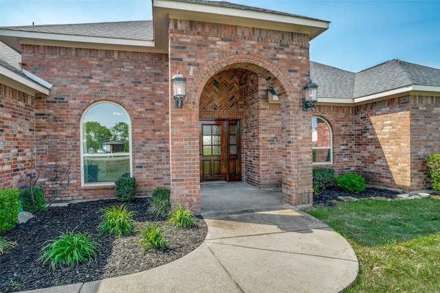 entrance to property featuring roof with shingles and brick siding