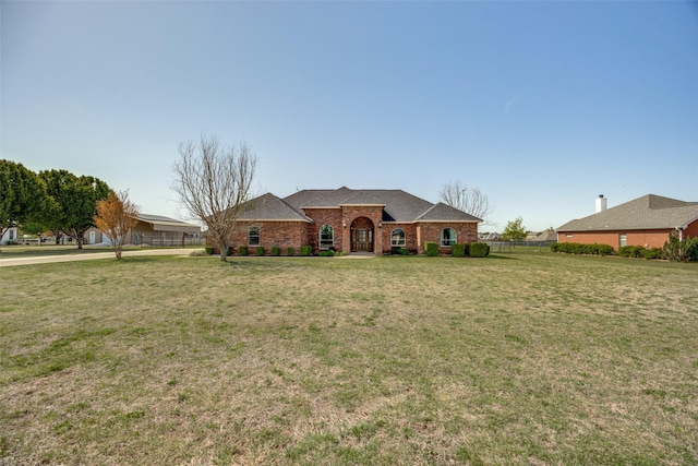 view of front of home with a front yard, fence, roof with shingles, and brick siding