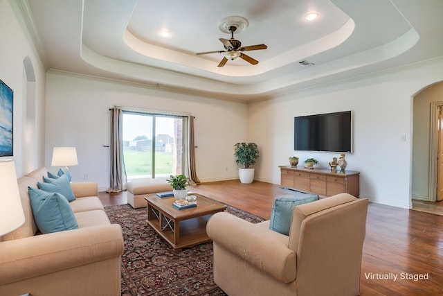 living area featuring visible vents, ceiling fan, a tray ceiling, arched walkways, and wood finished floors