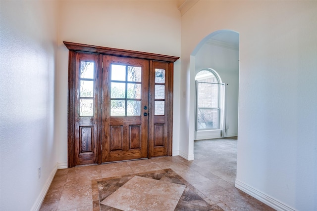 entrance foyer with baseboards, arched walkways, and a towering ceiling