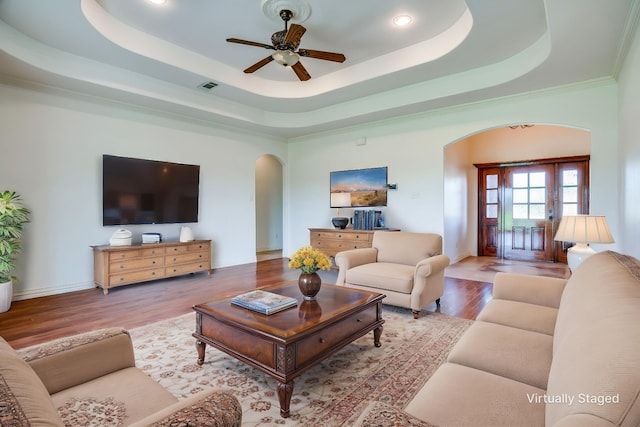 living room featuring a raised ceiling, visible vents, arched walkways, wood finished floors, and a ceiling fan