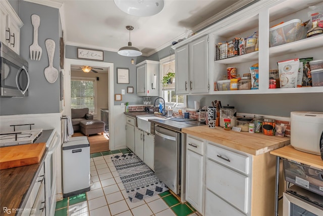 kitchen with light tile patterned floors, ornamental molding, wood counters, stainless steel appliances, and a wainscoted wall