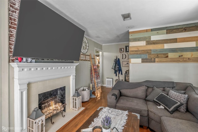 living room with visible vents, baseboards, a tiled fireplace, crown molding, and wood finished floors