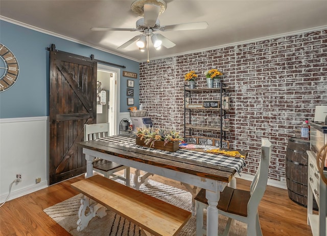 dining area with a barn door, brick wall, ornamental molding, a ceiling fan, and wood finished floors