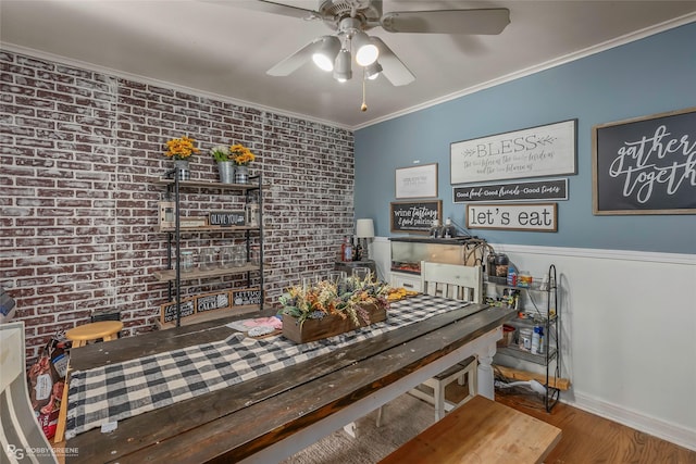 dining space with baseboards, brick wall, crown molding, ceiling fan, and wood finished floors