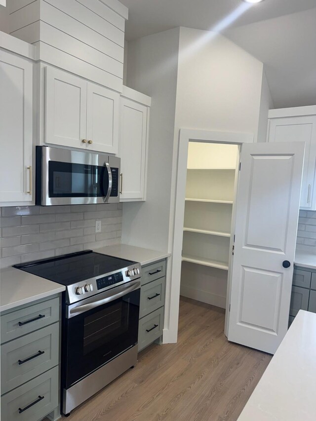 608 N Mill St, Weatherford, TX 76086 - kitchen with appliances with stainless steel finishes, light wood-style floors, light countertops, tasteful backsplash, and white cabinets