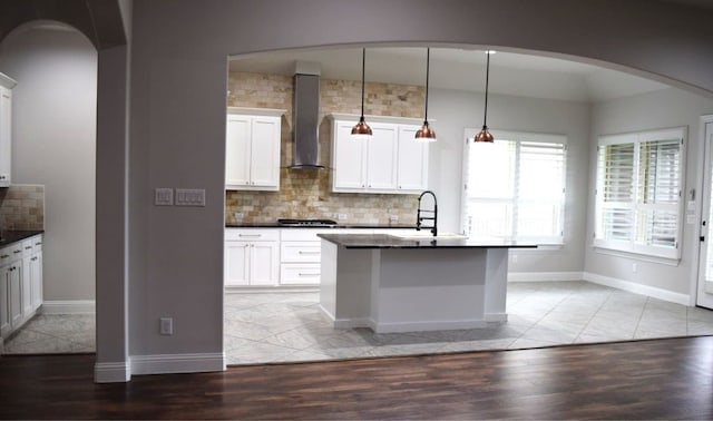 kitchen featuring wall chimney exhaust hood, a sink, dark countertops, stainless steel gas stovetop, and decorative backsplash