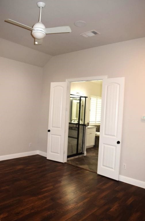 unfurnished bedroom with ceiling fan, dark wood-type flooring, visible vents, lofted ceiling, and baseboards