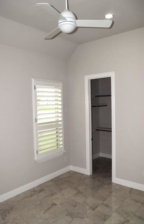 unfurnished bedroom with a closet, baseboards, a spacious closet, a ceiling fan, and vaulted ceiling