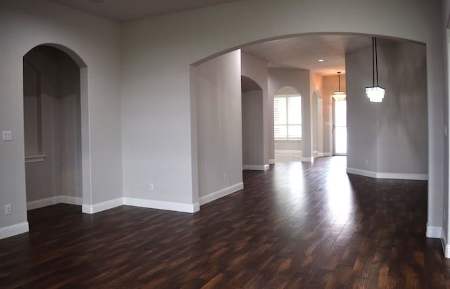 unfurnished room featuring arched walkways, dark wood-style flooring, and baseboards