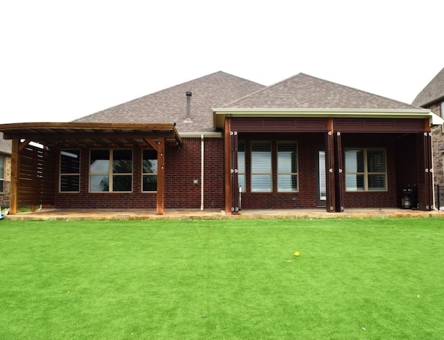 rear view of property featuring brick siding, a patio area, a lawn, and roof with shingles
