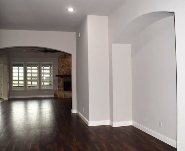 unfurnished living room with baseboards, a ceiling fan, arched walkways, and wood finished floors