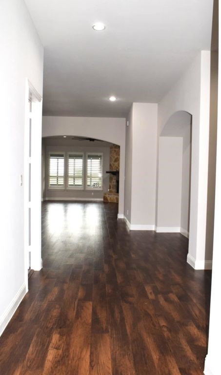 hall featuring arched walkways, baseboards, and dark wood-style floors