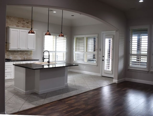 kitchen featuring arched walkways, white cabinets, a sink, dark countertops, and baseboards