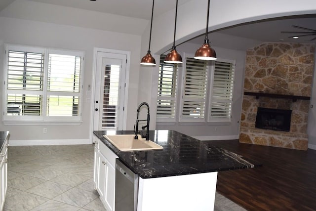 kitchen with baseboards, a fireplace, decorative light fixtures, stainless steel dishwasher, and a sink