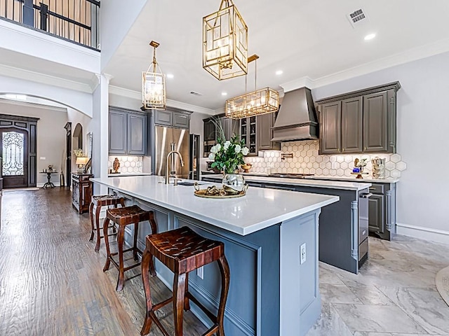 kitchen with arched walkways, tasteful backsplash, a spacious island, built in fridge, and premium range hood