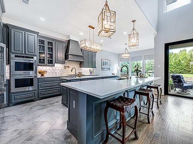 kitchen featuring a sink, a large island, a kitchen bar, custom range hood, and double oven