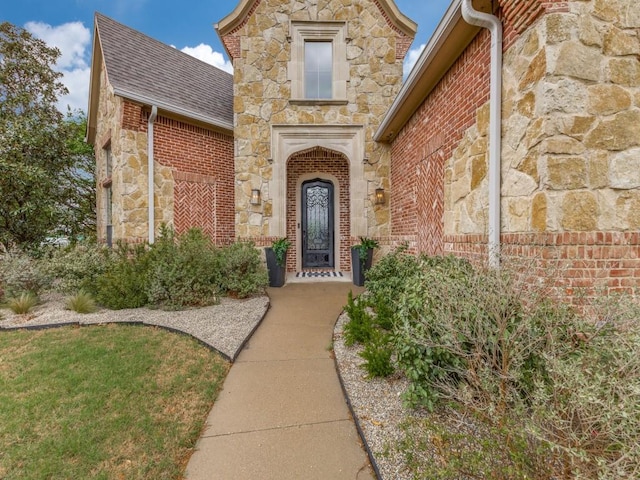 doorway to property featuring brick siding, stone siding, and a shingled roof