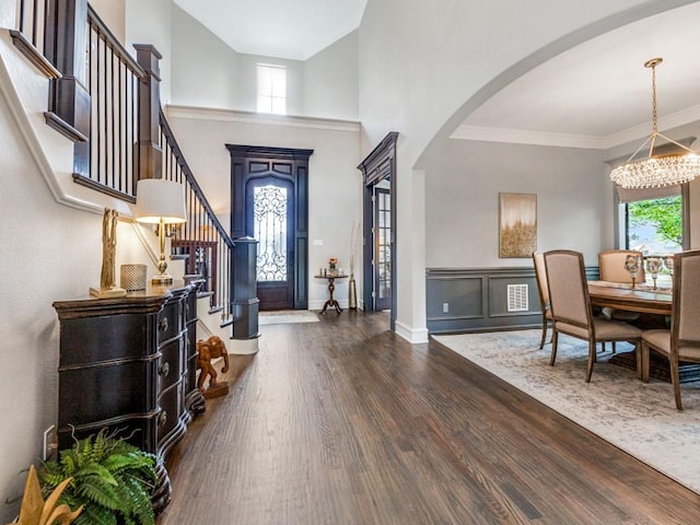 entrance foyer with arched walkways, a chandelier, a wealth of natural light, and dark wood-style flooring