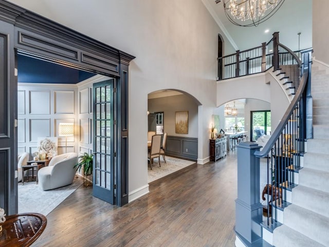 foyer entrance with arched walkways, wood finished floors, a chandelier, and a decorative wall