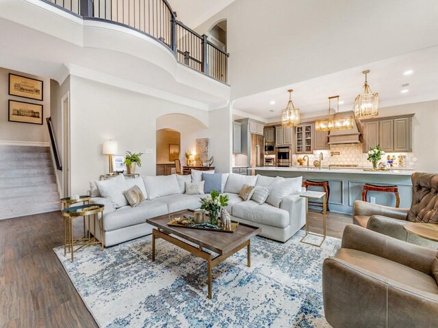 living area with arched walkways, dark wood finished floors, a high ceiling, and an inviting chandelier