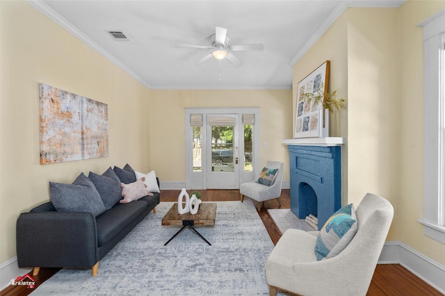 living area with a ceiling fan, crown molding, a fireplace with flush hearth, visible vents, and wood finished floors
