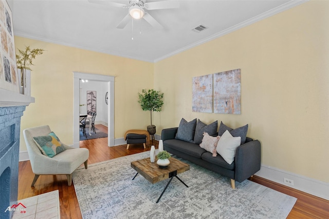 living room with crown molding, wood finished floors, a brick fireplace, and a ceiling fan