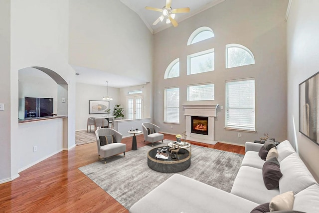 104 Bayonne Dr, Mansfield, TX 76063 - living room featuring ceiling fan, wood finished floors, arched walkways, high vaulted ceiling, and a warm lit fireplace