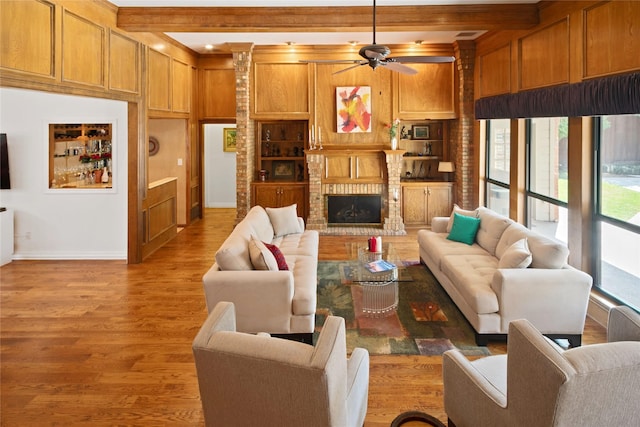 living area with built in shelves, ceiling fan, a fireplace, beamed ceiling, and light wood-style flooring
