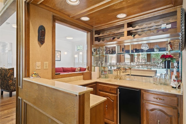 bar featuring crown molding, light wood-style flooring, refrigerator, wet bar, and a sink