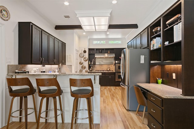kitchen featuring light stone counters, a peninsula, a kitchen bar, appliances with stainless steel finishes, and light wood finished floors