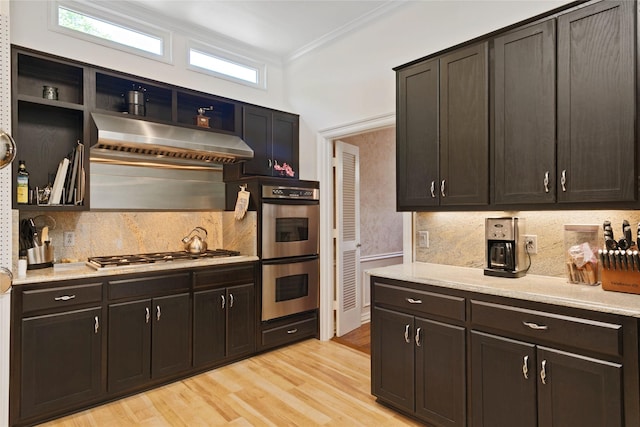 kitchen with ornamental molding, backsplash, under cabinet range hood, appliances with stainless steel finishes, and light wood finished floors