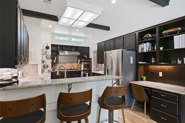 kitchen featuring tasteful backsplash, ornamental molding, under cabinet range hood, light stone countertops, and stainless steel appliances