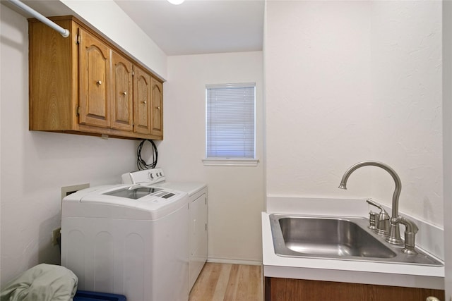 laundry area with light wood-style floors, separate washer and dryer, a sink, and cabinet space