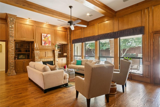 living area with built in features, wooden walls, a ceiling fan, beam ceiling, and wood finished floors
