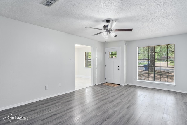 empty room featuring visible vents, a ceiling fan, baseboards, a textured ceiling, and dark wood-style flooring