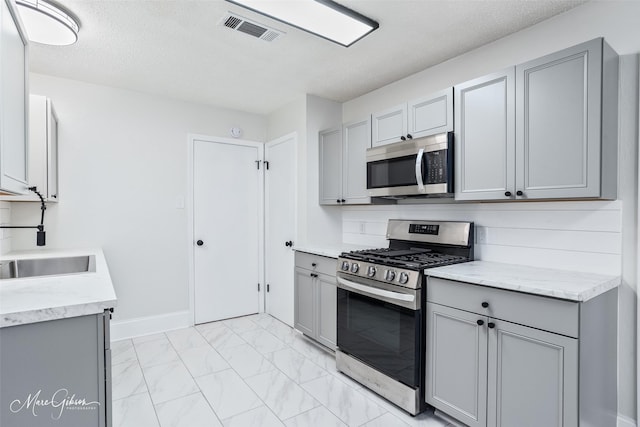 kitchen with stainless steel appliances, a sink, visible vents, gray cabinetry, and marble finish floor