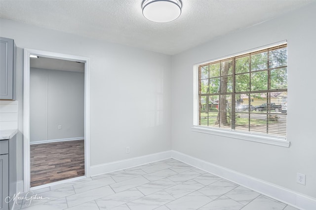 spare room with baseboards, marble finish floor, and a textured ceiling
