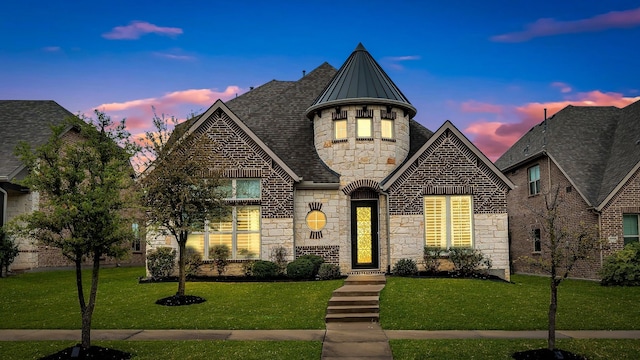 french country style house with a standing seam roof, a front yard, and stone siding