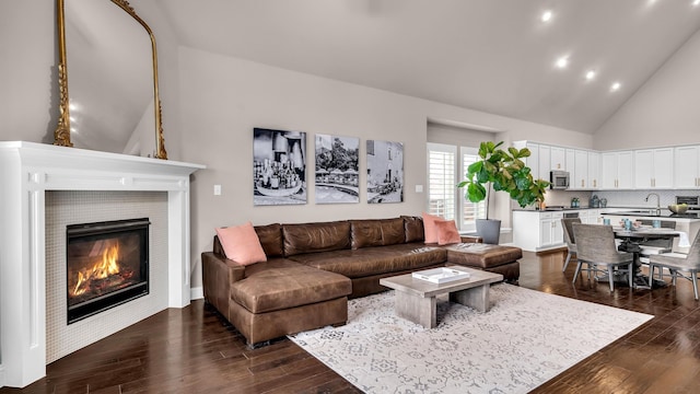 living area with dark wood-type flooring, high vaulted ceiling, and a tiled fireplace