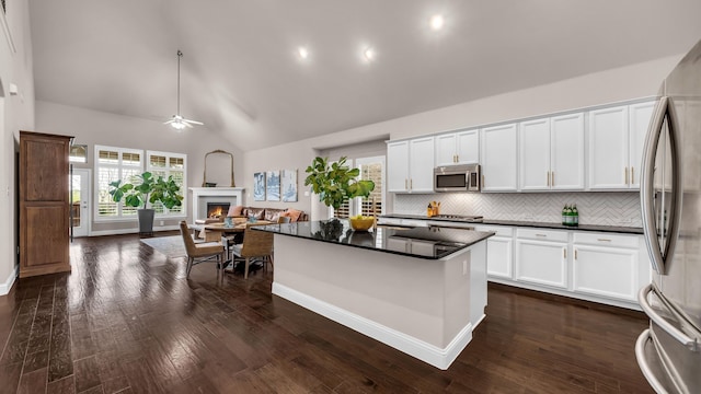 kitchen featuring a lit fireplace, open floor plan, white cabinetry, dark countertops, and stainless steel appliances