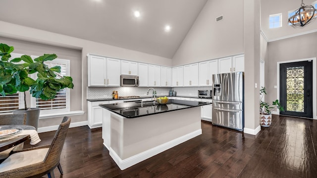 kitchen with white cabinets, dark countertops, an island with sink, stainless steel appliances, and high vaulted ceiling